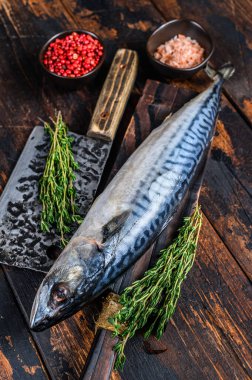 Taze çiğ balık uskumrusu bir satırla tahta bir kesme tahtasının üzerinde. Koyu ahşap arka plan. Üst görünüm.