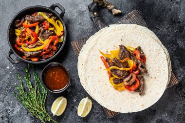 Biftek Fajitas, tortilla, biber ve soğan karışımı geleneksel Meksika yemekleri. Siyah arka plan. Üst görünüm.