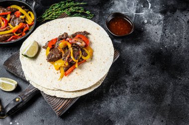 Meksika Fajitası, renkli biber ve soğanlı, tortilla ve salsa ile servis ediliyor. Siyah arka plan. Üst Manzara. Boşluğu kopyala.