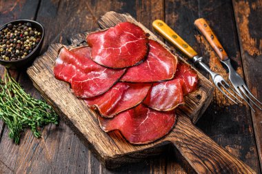 Italian Antipasti Bresaola cured meat beef cut pieces. Dark wooden background. Top view. clipart