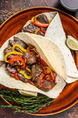 Fajitas Tortilla biftek şeritleri, tatlı biber ve soğanla sarılır. Karanlık ahşap arka plan. Üst görünüm.