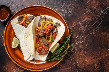 Fajitas Tortilla biftek şeritleri, tatlı biber ve soğanla sarılır. Karanlık ahşap arka plan. Üst Manzara. Boşluğu kopyala.