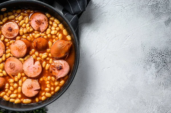 Stewed beans with smoked sausage and tomato sauce in a pan. White background. Top view. Copy space.