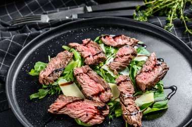 Ispanaklı biftek salatası, roka ve dilimlenmiş biftek. Siyah arka plan. Üst görünüm.