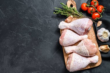 Tahta bir tahtanın üzerinde baharatlı ve sebzeli çiğ tavuk bacağı. Siyah arka plan. Üst Manzara. Boşluğu kopyala.