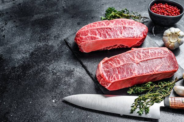 Raw top blade steak dry-aged on a stone board. Black background. Top view. Copy space.