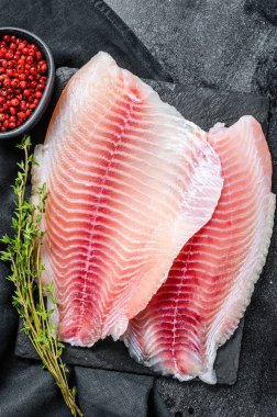 Kekik ve pembe biberli çiğ tilapia fileto. Siyah arka plan. Üst görünüm.