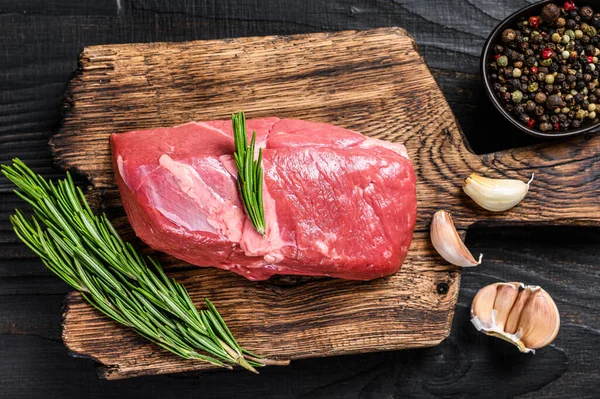 Tahta kesme tahtasında taze çiğ sığır filetosu bifteği. Siyah ahşap arka plan. Üst görünüm.