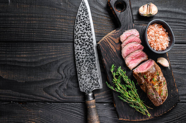 Grilled lamb tenderloin meat steak on a meat cleaver. Black wooden background. Top view. Copy space.