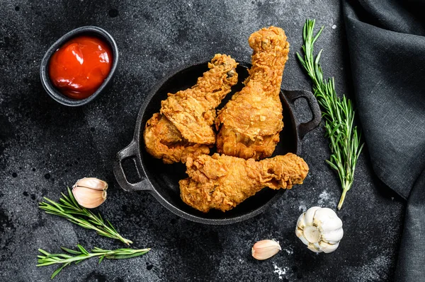 Fried crispy chicken legs, drumstick in a pan. Black background. Top view.