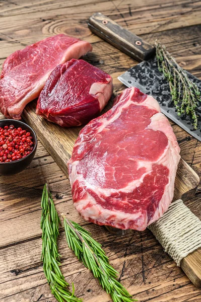 Variety of raw black angus beef meat steaks fillet Mignon, rib eye or cowboy, Striploin or new york. Wooden background. Top view.