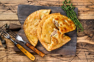 Tahta kesme tahtasının üzerinde servis edilen kıymalı et ile dolu Şili usulü kızarmış börekler. Ahşap arka plan. Üst görünüm.