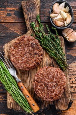 Tahta bir kesme tahtasının üzerinde kıyma etinden hamburger için ızgara biftek köftesi. Koyu ahşap arka plan. Üst görünüm.