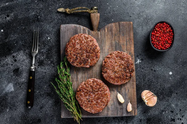 Churrasco grelhado carne de vaca rissóis para hambúrguer de carne picada e ervas em uma placa de madeira. Fundo preto. Vista superior — Fotografia de Stock