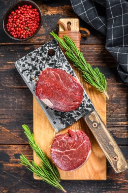 Kesme tahtasında çiğ mermer et fileto mignon. Karanlık ahşap arka plan. Üst görünüm.