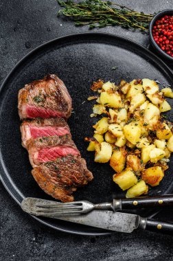 Izgara Striploin bifteği, patates ve sığır eti. Siyah arka plan. Üst görünüm.
