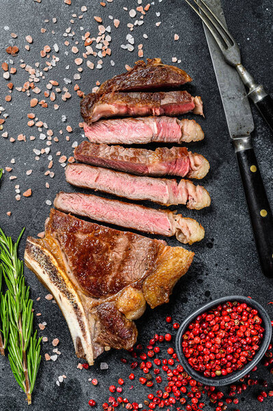 Ribeye steak on the bone with salt and pepper. Grilled Beef meat. Black background. Top view.