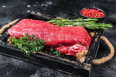 Tahta tepside otlarla dolu çiğ sığır filetosu eti. Siyah arka plan. Üst görünüm.