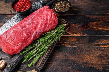 Biftek fileto için bütün çiğ bonfileto eti kasap bıçağıyla ahşap bir kesme tahtasının üzerinde. Koyu ahşap arka plan. Üst Manzara. Boşluğu kopyala.