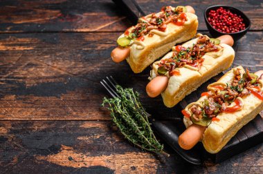 Sosisli sandviçler tamamen kızarmış pastırma, soğan ve salatalık turşusuyla dolu. Koyu ahşap arka plan. Üst Manzara. Boşluğu kopyala.