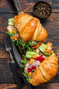 Ahşap doğrama tahtasının üzerinde jambon ve marulla dolu kruvasan. Siyah arka plan. Üst görünüm.