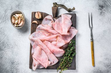 İnce jambonlu ahşap kesim tahtasında otlarla dilimlenmiş. Beyaz arka plan. Üst görünüm.