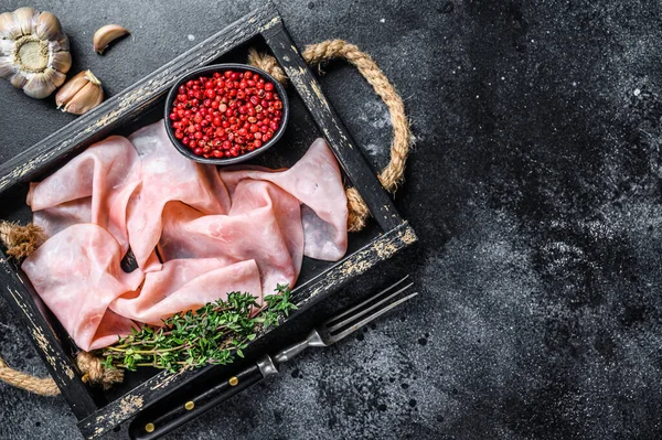 Thin sliced Smoked pork ham in wooden tray. Black background. Top view. Copy space.