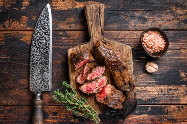 Ahşap bir tahtanın üzerinde ızgara bonfile biftek dilimleri. Koyu ahşap arka plan. Üst görünüm.