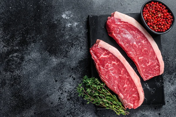 Çiğ biftek ya da mermer tahtada sığır eti bifteği. Siyah arka plan. Üst Manzara. Boşluğu kopyala.