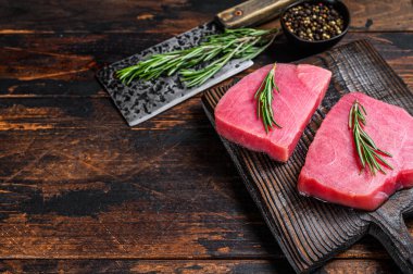 Tahta kesme tahtasında satırla çiğ ton balığı bifteği. Koyu ahşap arka plan. Üst Manzara. Boşluğu kopyala.