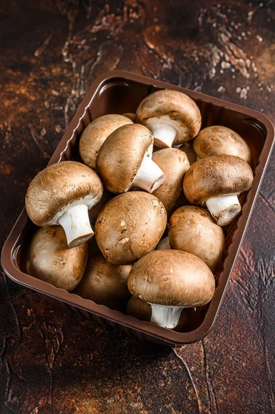 Raw Fresh champignon mushrooms in a plastic box. Dark background. Top view
