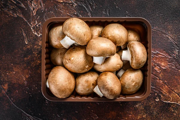 Raw Fresh champignon mushrooms in a plastic box. Dark background. Top view