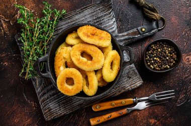 Kesme tahtasının üzerinde kızarmış mürekkep balığı halkaları. Karanlık arka plan. Üst görünüm.