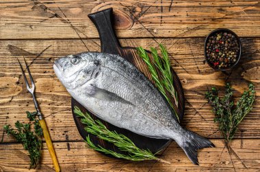 Çiğ deniz kepeği ya da kesme tahtasındaki baharat ve otlu dorado balığı. Ahşap arka plan. Üst görünüm