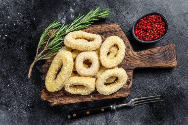 Kesme tahtasındaki ekmek kırıntıları içinde çiğ kalamar halkaları. Siyah arka plan. Üst görünüm.