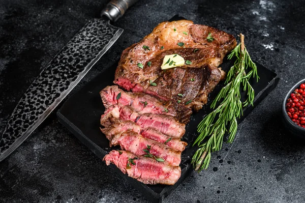 Cut Grilled Chuck eye roll beef meat steak on a marble board. Black background. Top view