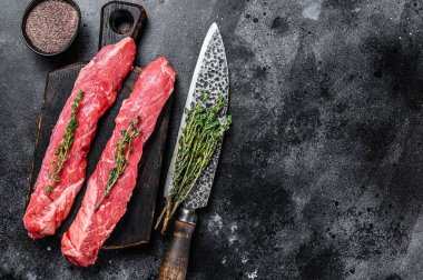 Kesme tahtasının üzerinde bıçakla kesilmiş çiğ etekli biftek. Siyah arka plan. Üst Manzara. Boşluğu kopyala