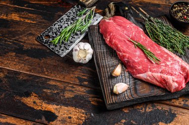 Kesme tahtasının üzerinde satırla birlikte çiğ etekli biftek. Koyu ahşap arka plan. Üst Manzara. Boşluğu kopyala