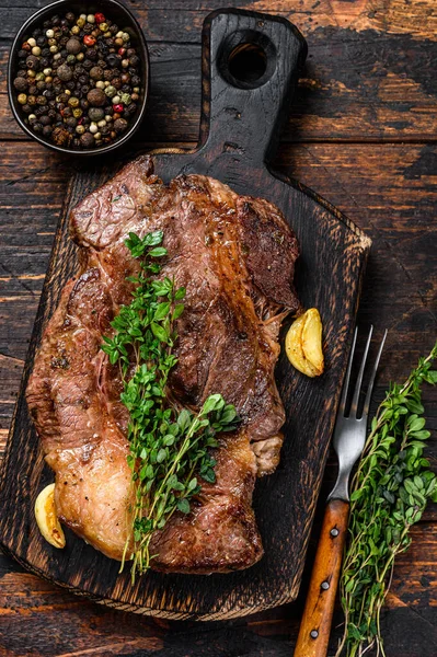 Grilovaný hovězí steak z Chuckových očí na prkně. Tmavé dřevěné pozadí. Horní pohled — Stock fotografie