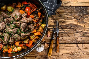 Biftek eti ve sebze yahnisi siyah fırın kabında. Ahşap arka plan. Üst Manzara. Boşluğu kopyala