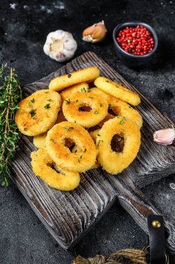 Kesme tahtasının üzerinde kızartılmış kalamar halkaları. Siyah arka plan. Üst görünüm.