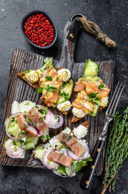 Krem peynirli ve salatalı füme somon ve ringa balığı sandviçi. Siyah arka plan. Üst görünüm.