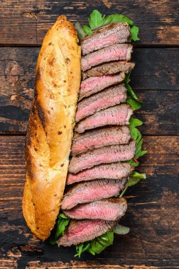 Roka ve peynirli ızgara baget biftekli sandviç. Koyu ahşap arka plan. Üst görünüm.