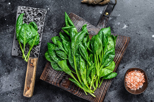 Raw fresh young baby spinach leaves on a wooden cutting board. Black background. Top view