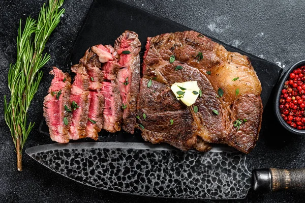 Cut Grilled Chuck eye roll beef meat steak on a marble board. Black background. Top view