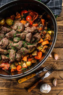 Biftek eti ve sebze yahnisi siyah fırın kabında. Ahşap arka plan. Üst görünüm