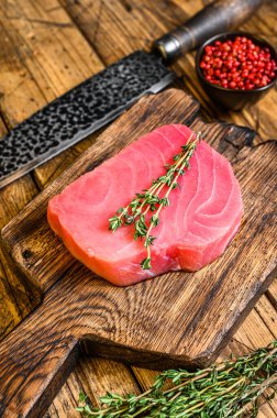 Tahta kesme tahtasında bıçakla taze çiğ ton balığı bifteği. Ahşap arka plan. Üst görünüm.