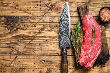 Kesme tahtasının üzerinde bıçakla kesilmiş çiğ etekli biftek. Ahşap arka plan. Üst Manzara. Boşluğu kopyala