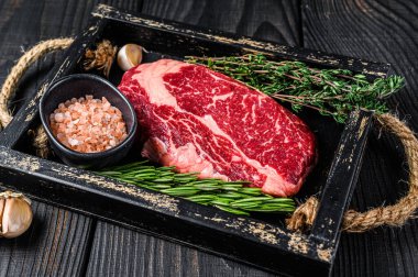 Ham pirzola bifteği kasap ahşap tepside otlarla birlikte. Siyah ahşap arka plan. Üst görünüm