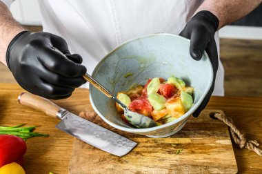 Siyah eldivenli bir şef vejetaryen sebze salatası hazırlıyor. Sağlıklı organik gıda pişirme kavramı